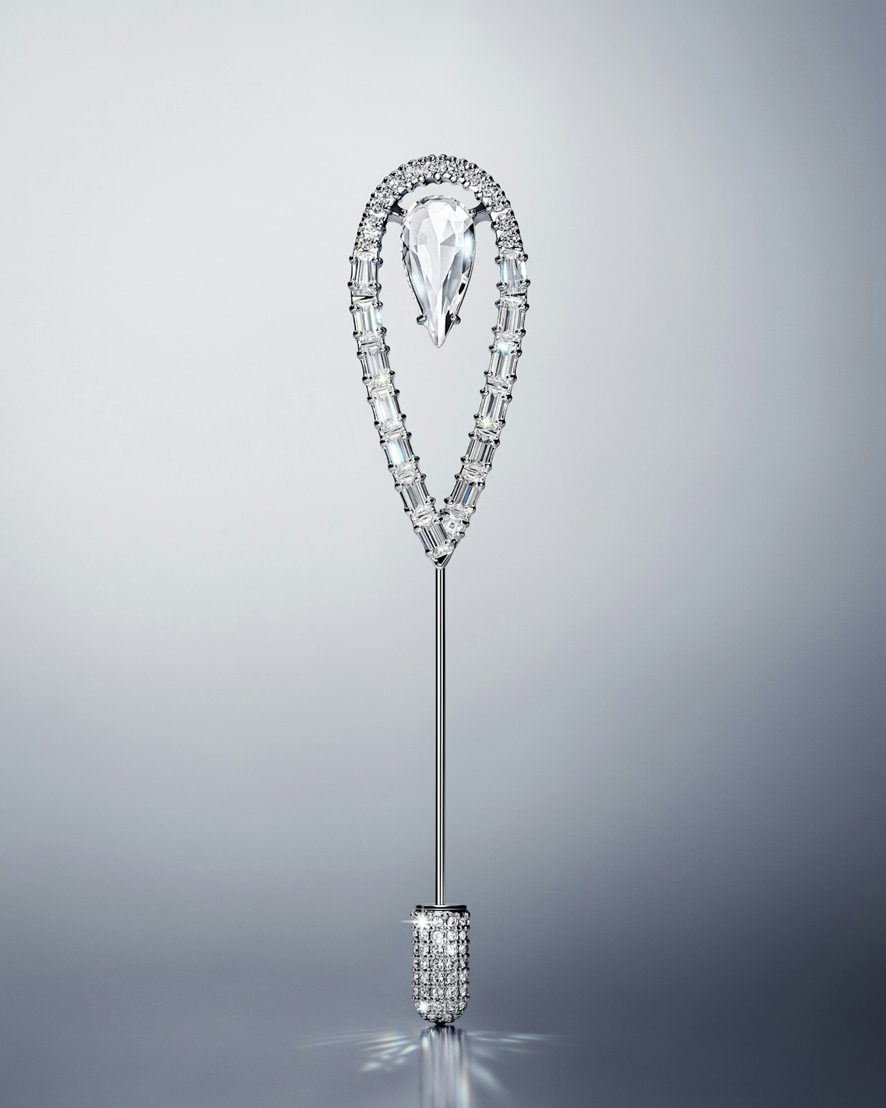 A jeweled pin with a teardrop-shaped diamond and silver accents on a gray background.