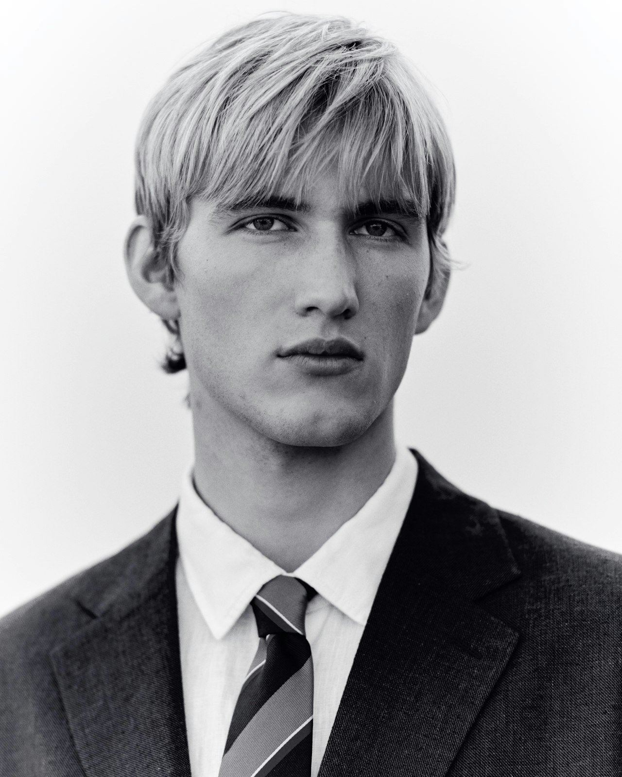 Young man in a suit and tie with light hair, looking seriously at the camera.