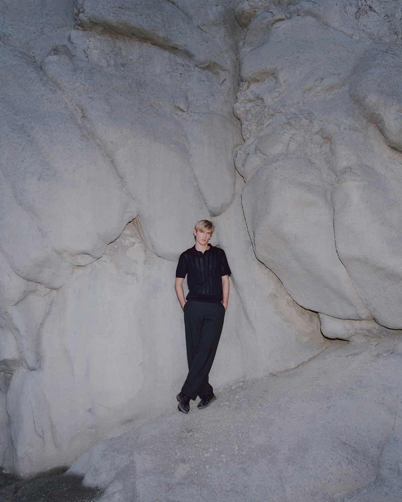 Person in black clothing stands against large, light-colored rock formation.