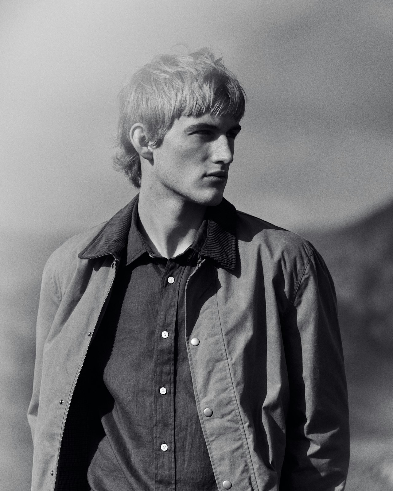 Black-and-white photo of a man in a button-up shirt and jacket, looking away.
