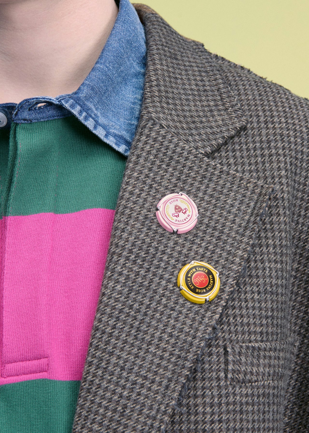 Close-up of a blazer with two colorful pins on the lapel over a striped shirt.