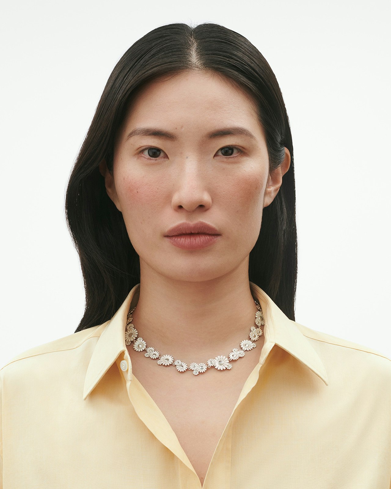Woman in a yellow shirt wearing a floral necklace, looking directly at the camera.