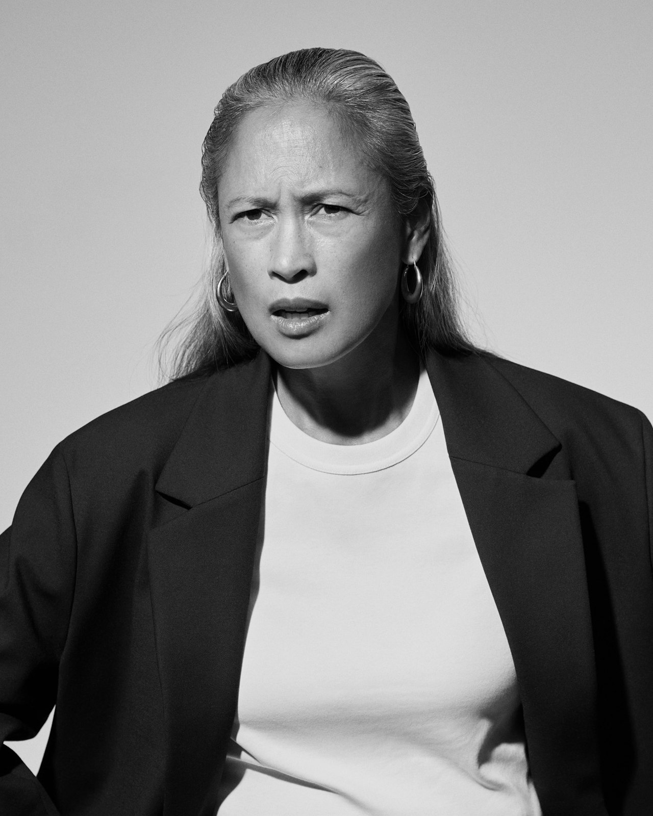 A person with long hair looks confused, wearing a blazer over a t-shirt.
