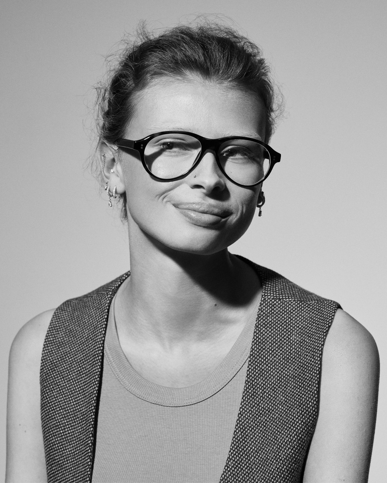 Black and white portrait of a woman wearing glasses and a sleeveless vest, smiling.