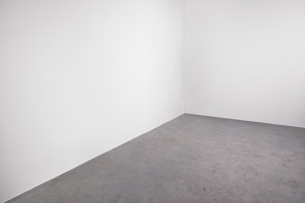 An empty room with plain white walls meeting at a corner and a bare gray concrete floor.