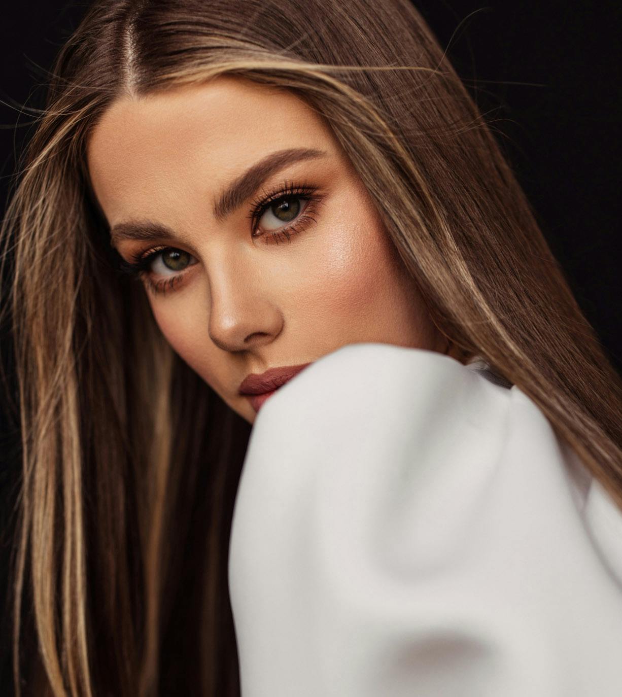 woman with long straight brown hair looking over her shoulder