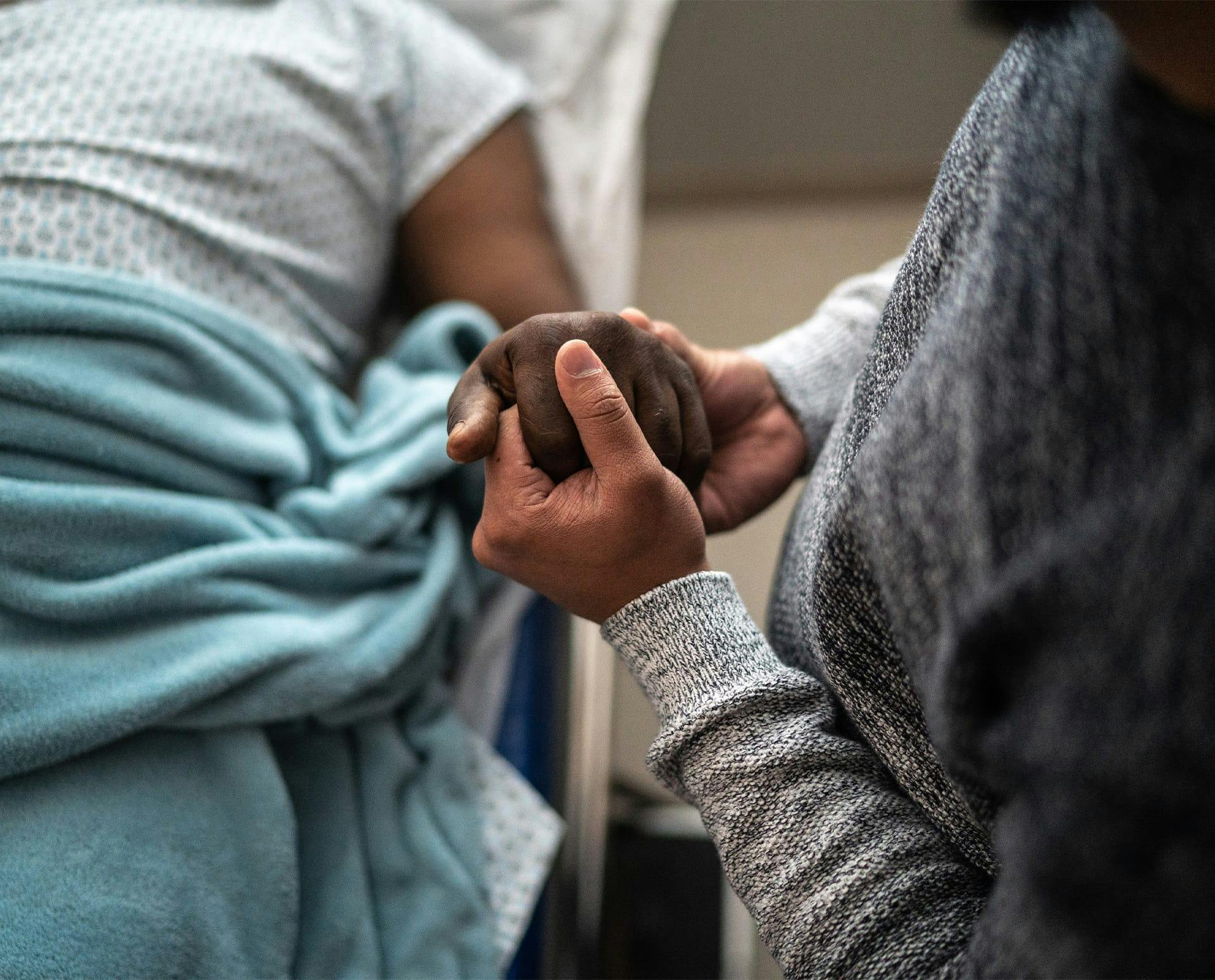 person holding another's hand while they lay in hospital bed