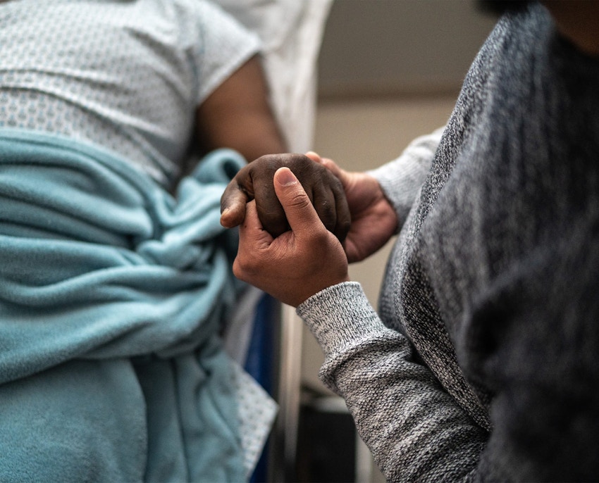 person holding another's hand while they lay in hospital bed