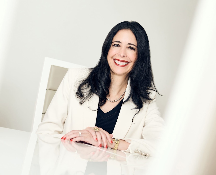 Hella sitting at table with her hand over the other