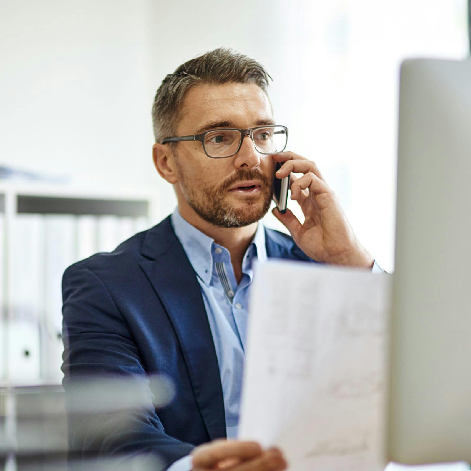 man in glasses on the phone while holding up paper