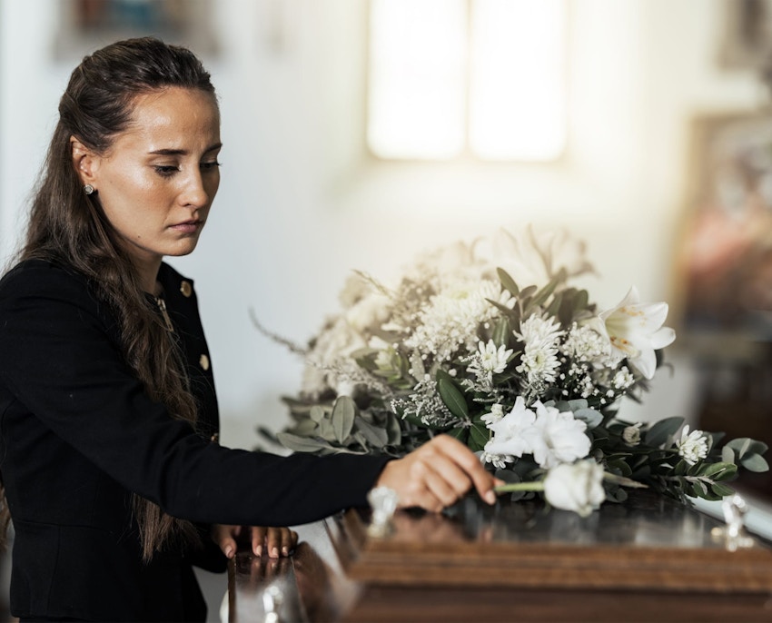 Woman standing over casket putting flower on it