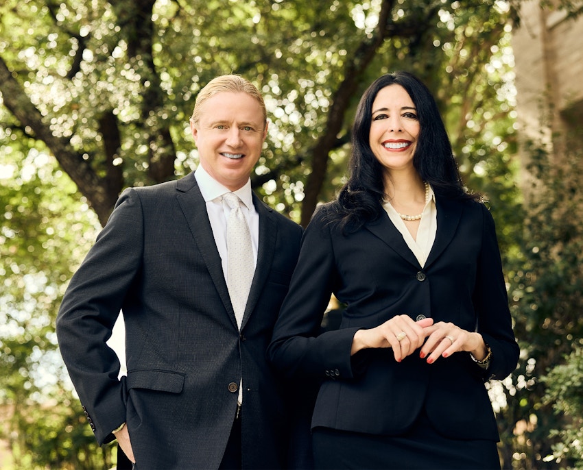 Tyler and Hella in black suits in front of tree