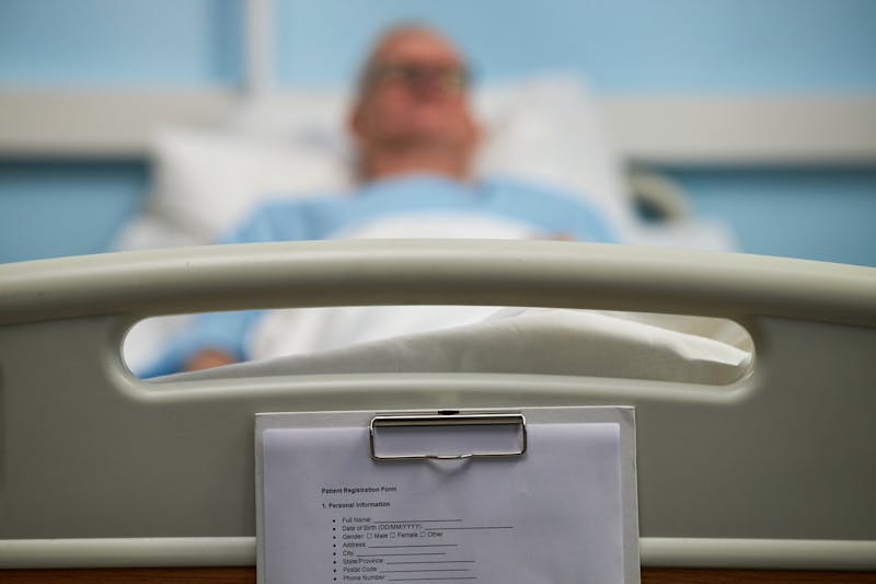man on hospitla bed with a clipboard at the end of the bed