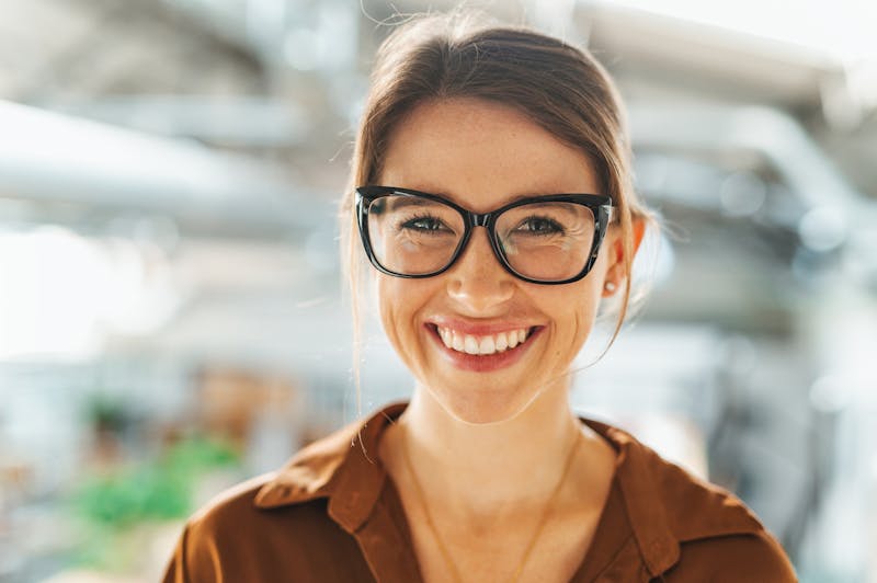 Woman standing in natural light smiling and wearing glasses.