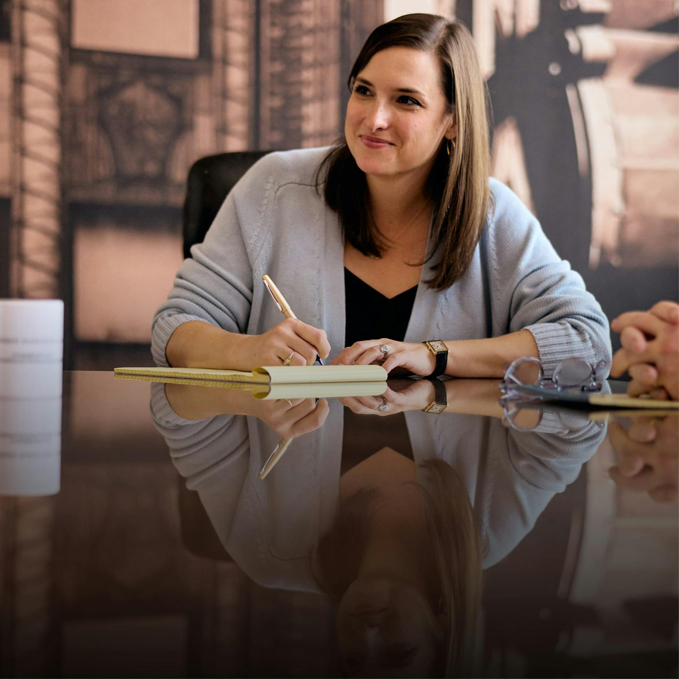 Woman sitting at a conference table, taking notes on paper.