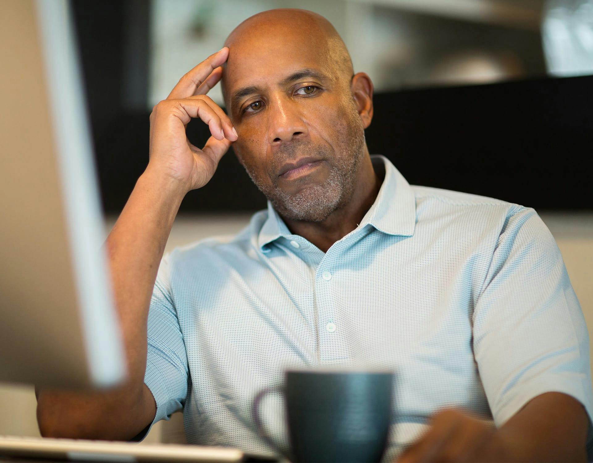 man touching his head, sitting at a desk