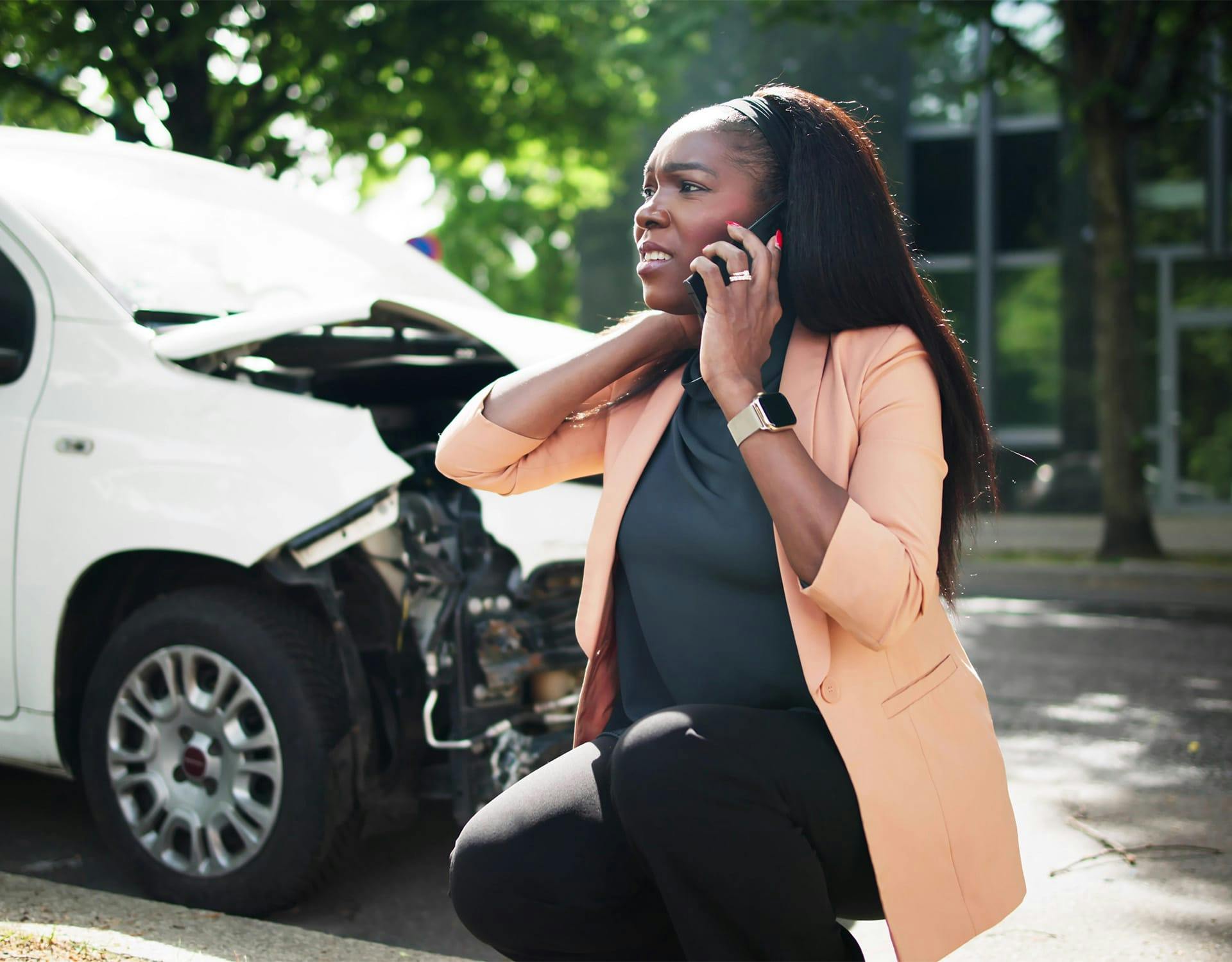 woman on the phone, sitting next to a wrecked car