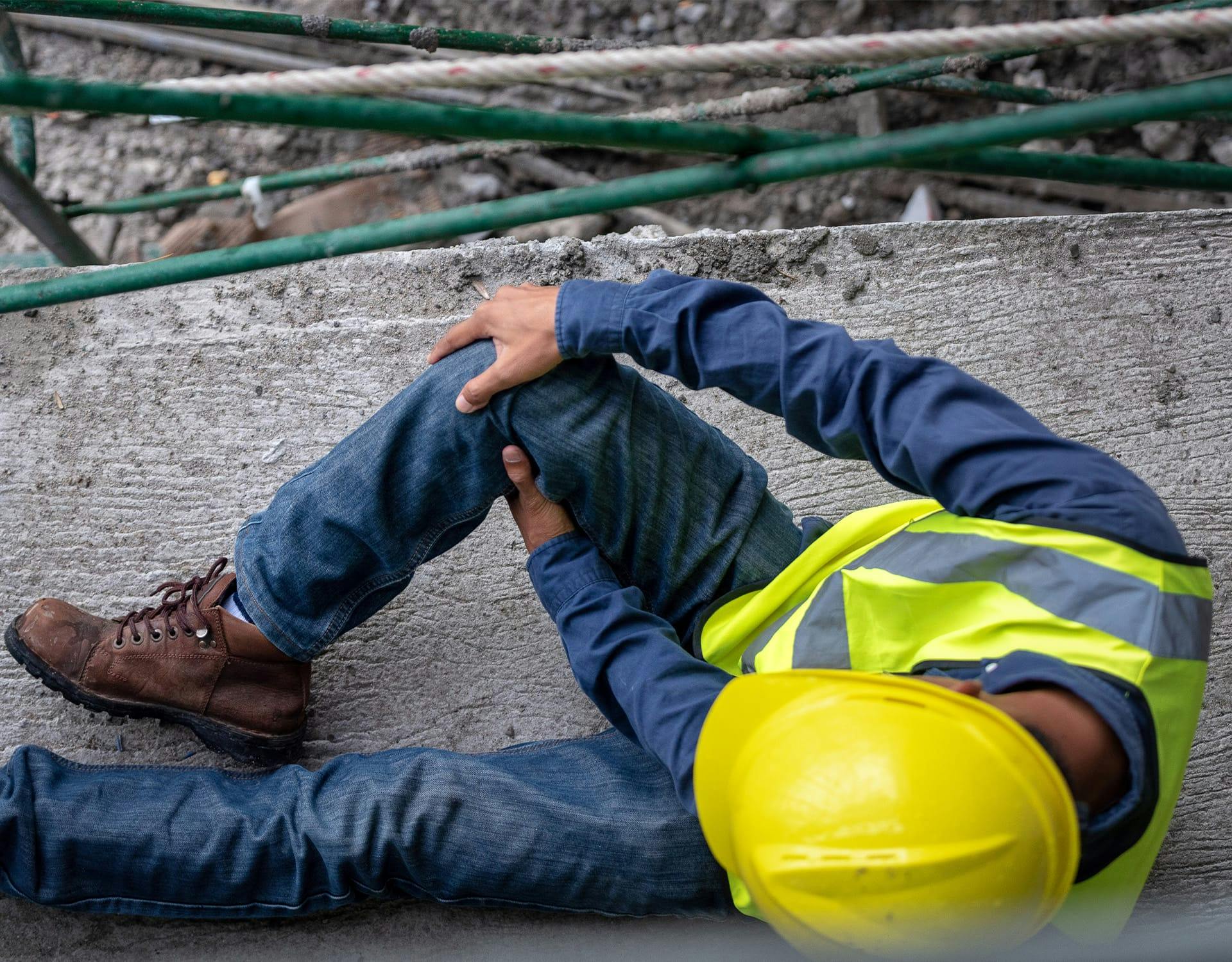 man in a construction uniform on the ground holding his knee