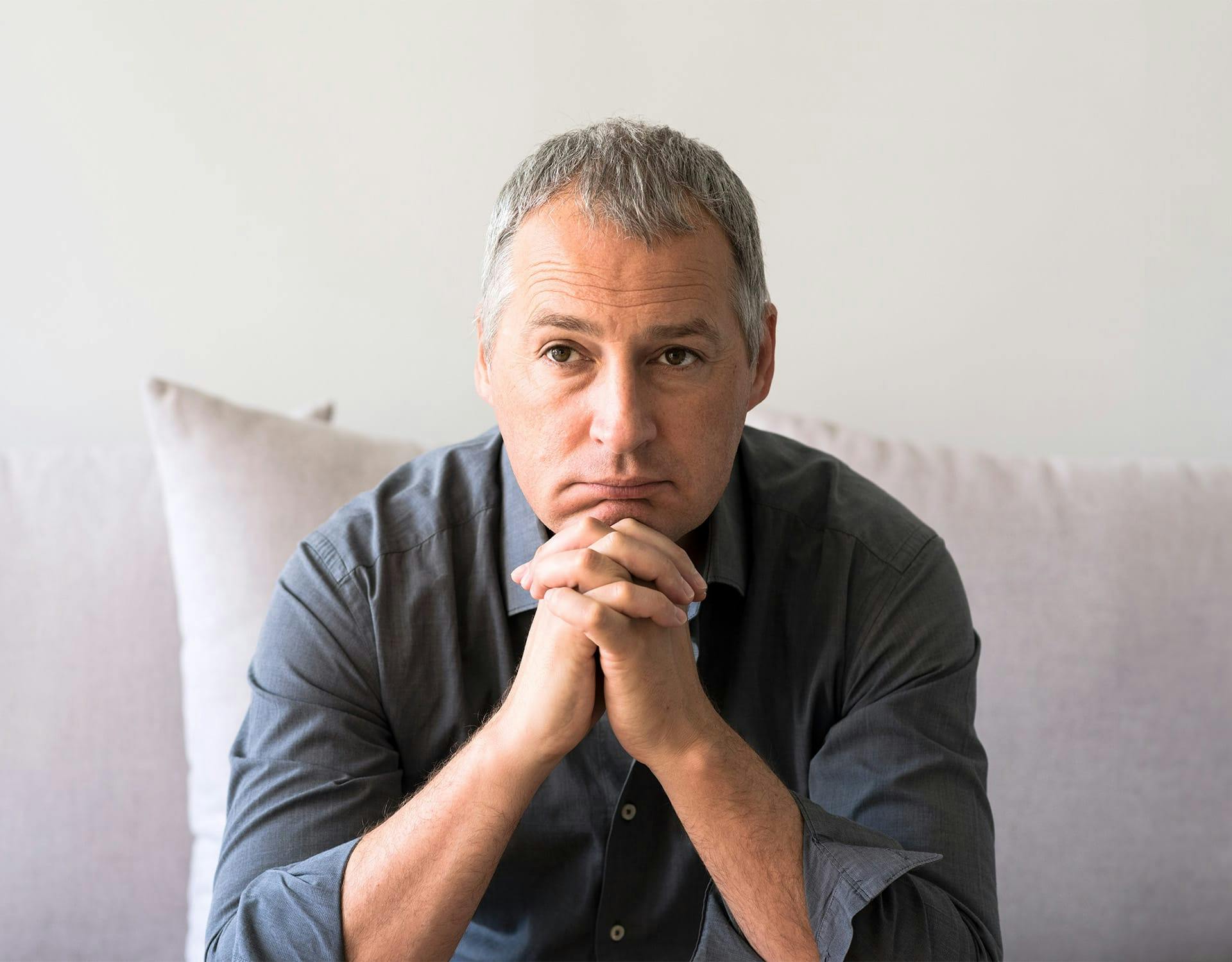man sitting on a couch, resting his chin on his hands
