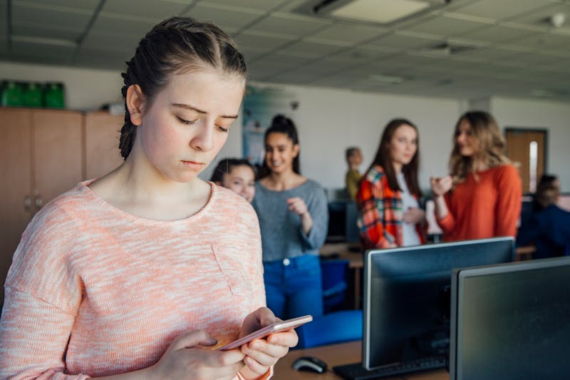 girl at school looking at her phone while other girls point at her