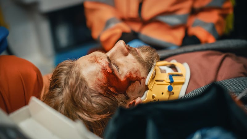 man laying down wearing a neck brace with blood on face
