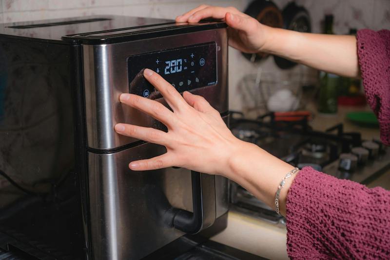 A woman in her kitchen is programming her air fryer to fry chicken wings.
