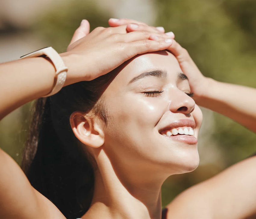 Woman smiling with hands on head out in the sun