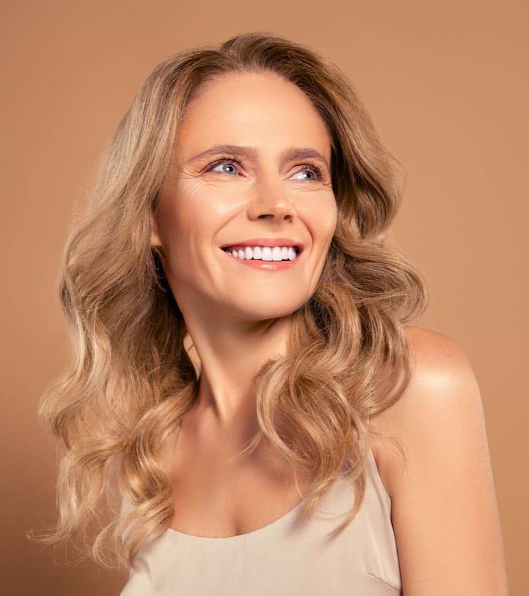 Older woman with long wavy hair smiles looking away from the camera in a studio shoot. Her youthful appearance despiter her age is to show the potential results of a neck lift in Bellevue with NewSkin