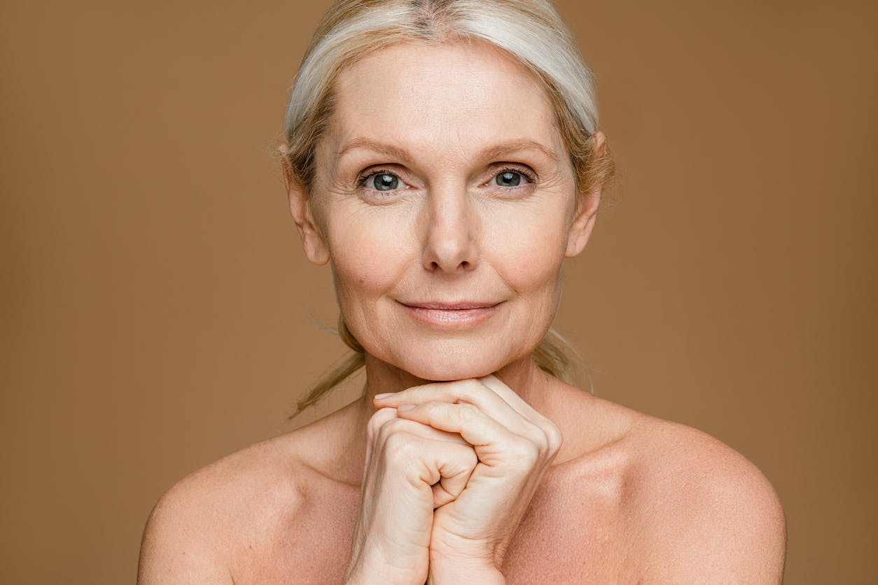 Older woman smiles at camera in a studio shoot. Her bright eyes emulate the potential results of a blepharoplasty in Bellevue