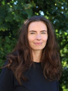 A person with long brown hair and blue eyes, subtly smiling.