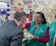 A woman in a green vest showing jewelry to a man in a suit.