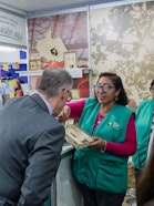 A woman in a green vest showing jewelry to a man in a suit.