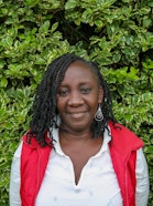 A woman with braids in a red west and white shirt smiling.