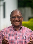 A person with glasses in a plaid shirt smiling and putting their hands forward