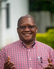 A person with glasses in a plaid shirt smiling and putting their hands forward