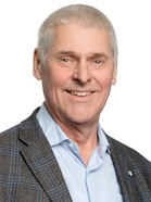 A portrait of a man in a plaid suit jacket smiling