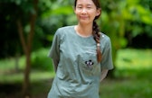 A woman in medical clothing smiling in a nature setting