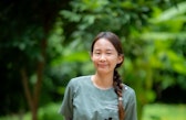 ine Frau in medizinischer Kleidung lächelt in einer Naturumgebung