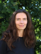 A woman with long brown hair and blue eyes in a nature setting