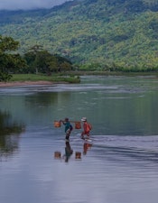 Two residents wade across a river in northeastern Madagascar, carrying goods on a pole between villages and fields.