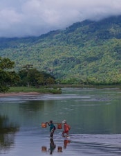 Dorfbewohner*innen durchqueren einen Fluss im Nordosten Madagaskars und transportieren Güter.