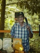 Ein älterer Mann im karierten Hemd und mit Mütze hält eine Machete über der Schulter, neben einer Auslage mit gerahmten Fotografien, Urkunden und Naturschutz-Auszeichnungen.