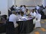 Several small groups seated at round tables in discussion in a workshop room; a participant in a Kenya jersey in the foreground.