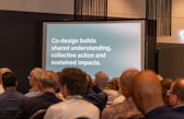 Presentation slide reading “Co-design builds shared understanding, collective action and sustained impacts,” viewed from the audience.