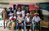 Eine Gruppe posiert im Mirohy Center in Ankovana; einige Personen sitzen, andere stehen dahinter. Viele tragen helle Hüte mit breiter Krempe. Links und rechts sind Banner der Full Circle Initiative und der Wyss Academy zu sehen.