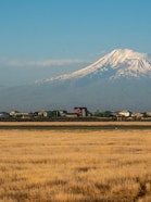Scenic panoramic view of the majestic snow-capped Mount Ararat and Little Ararat rising above rural houses, captured from Zvartnots International Airport