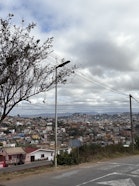 View across the densely built hills of Antananarivo beneath a cloudy sky, with a roadside tree, streetlights, and power lines in the foreground.