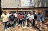 Julie Zähringer and ten workshop participants stand together in front of a brick building beneath a sign reading “École Doctorale GRND – Université d’Antananarivo.”