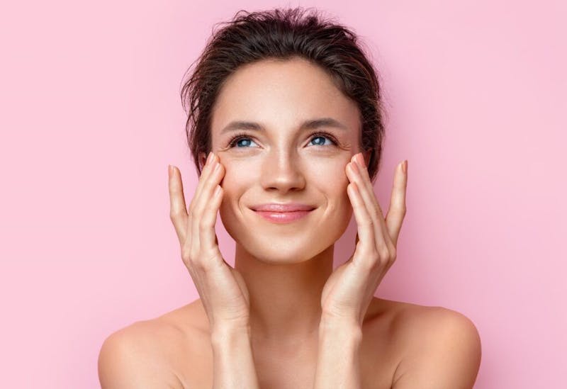 A woman against a pink background touching her face