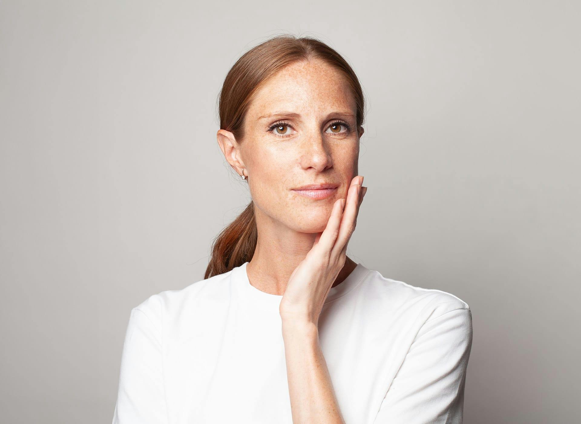 woman in white shirt touching her jaw with low ponytail